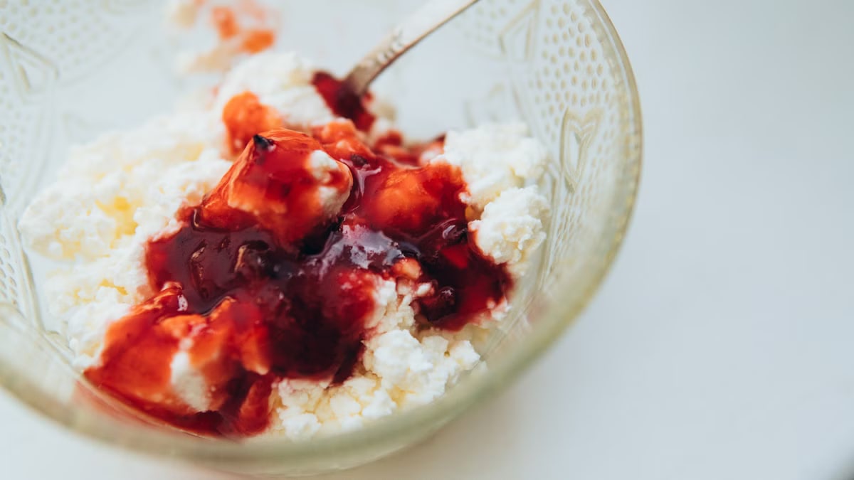 From above of appetizing cottage cheese with berry jam served in glass bowl with spoon on white table